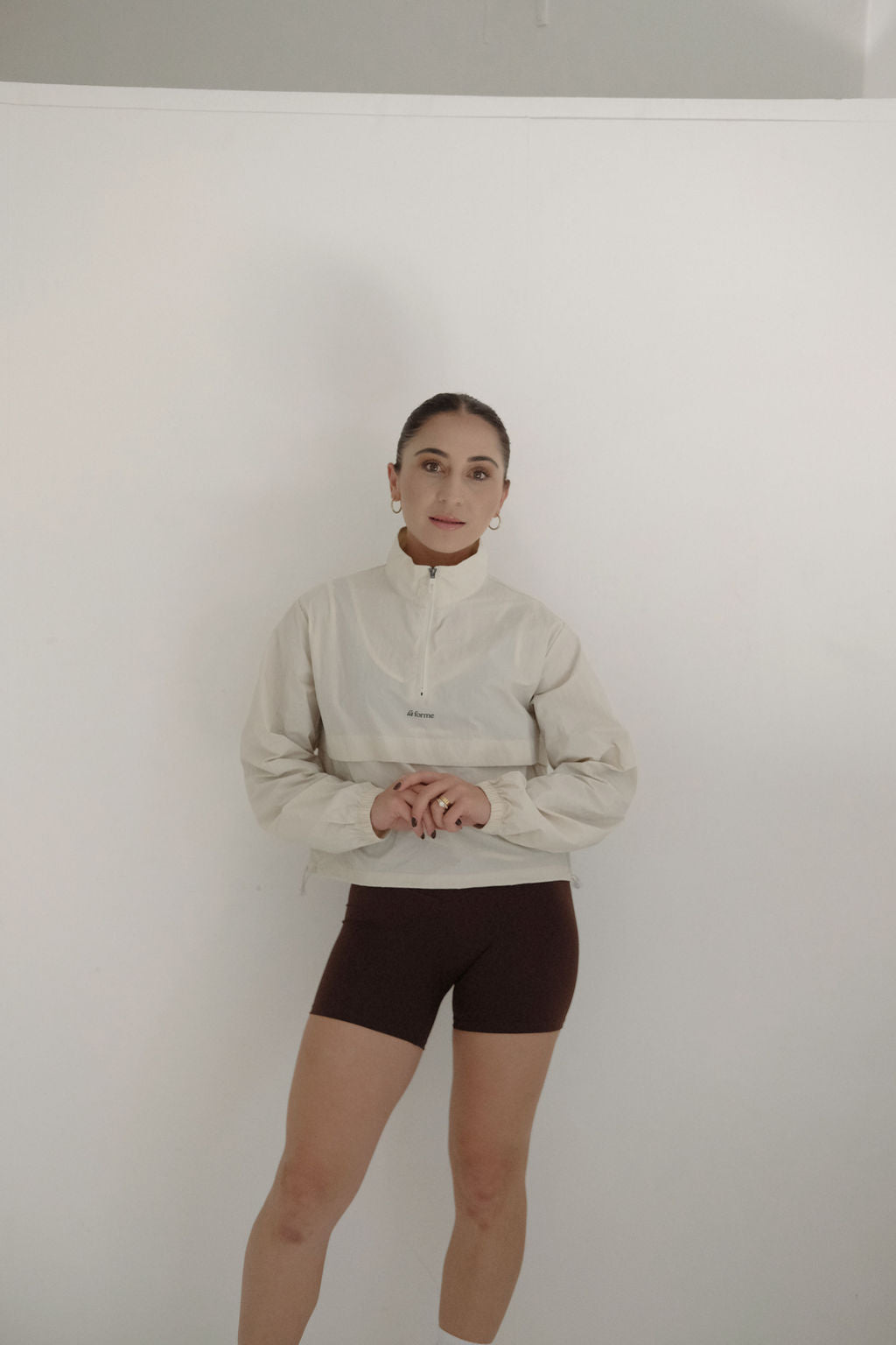Person wearing a beige jacket and brown shorts against a white background
